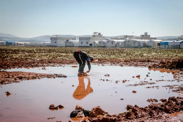 A little boy standing on a rock in the middle of a puddle.